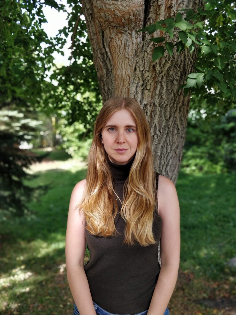 Calgary Therapist Stephanie Jones in nature. Stephanie is a white female with blonde hair and green eyes and is looking into the camera. Stephanie works with Individuals, Trauma, Children, and Couples